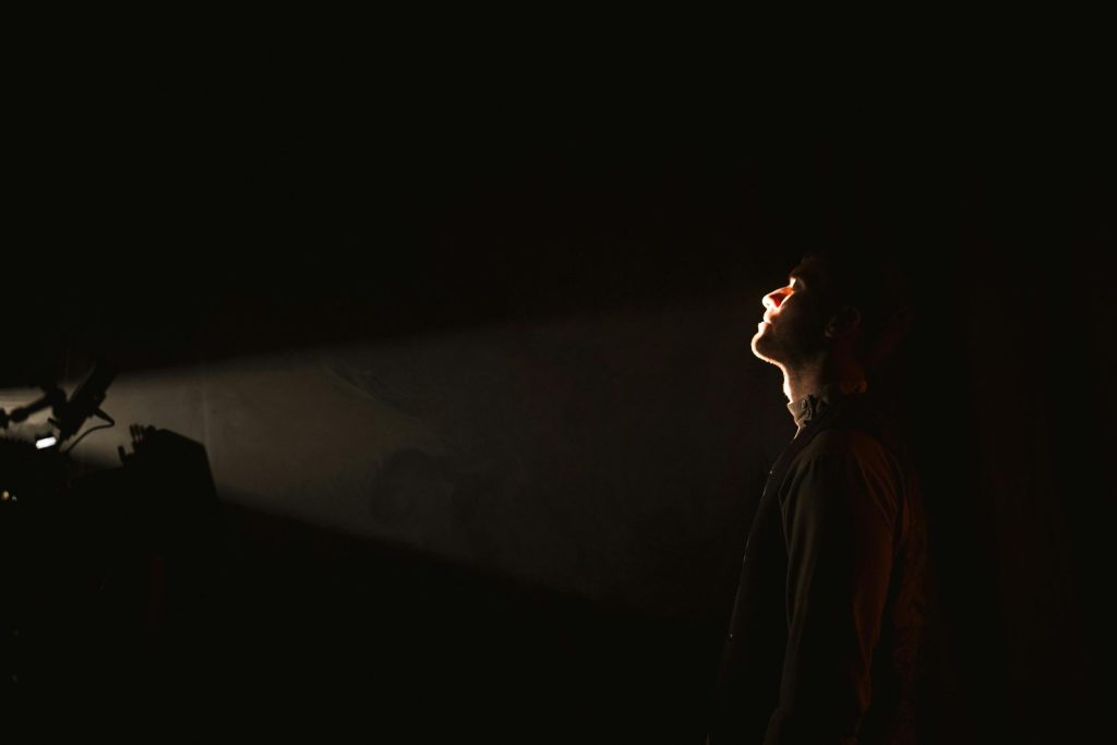 A man stands in darkness with a spotlight illuminating his face, creating a dramatic effect.