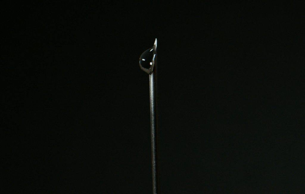 Close-up of a steel needle with a water droplet against a dark background.